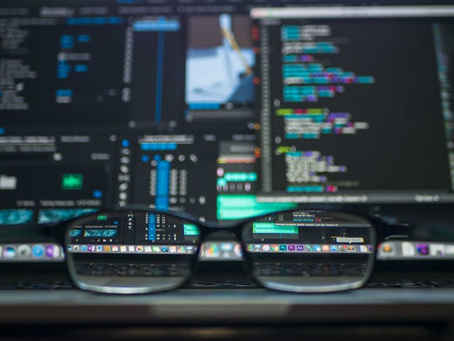プログラマー プログラミングのコードが書かれたスクリーンとパソコンの前に置かれた眼鏡
