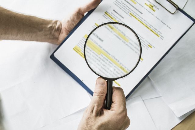 虫眼鏡を使って書類の要件を確認している男性