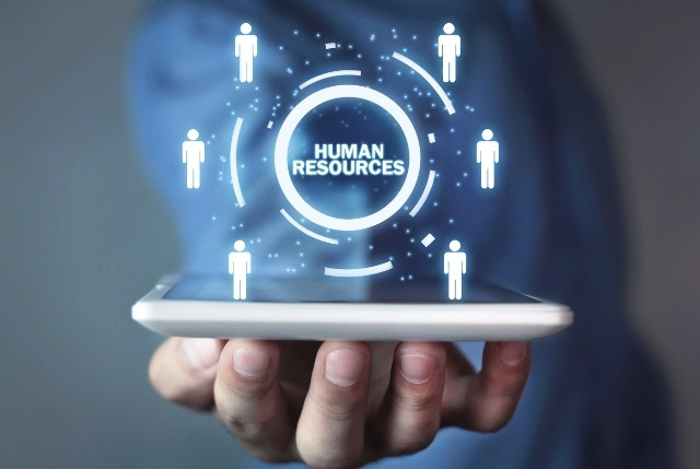 手のひらに置かれたスマートフォンの上に、人事管理を示す「HUMAN RESOURCES」のデジタルアイコンが浮かんでいる様子