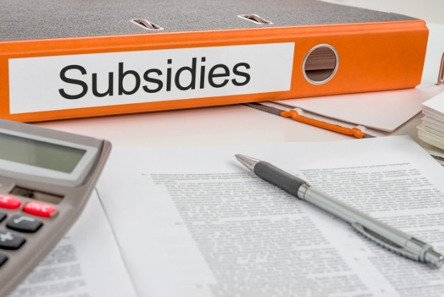 “Subsidies”とラベルされたオレンジ色のファイルバインダーと、机の上に置かれた書類・ペン・電卓のクローズアップ