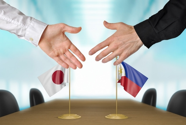 フィリピンと日本の国旗の前で握手をしている場面