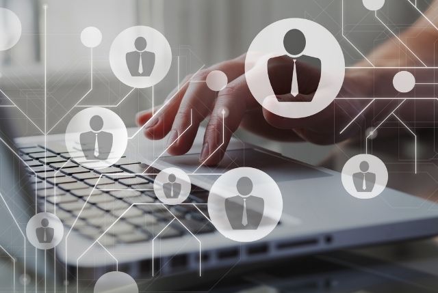 ノートパソコンでタイピングする手と、人材やビジネスネットワークを象徴するアイコンのイメージ