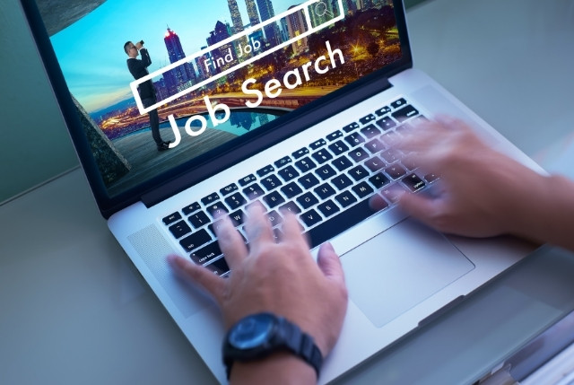 ノートパソコンの画面に「Job Search」と表示され、手がキーボードを打つ様子。外国人材を含む求職者が仕事を探すオンライン就職活動のイメージ。